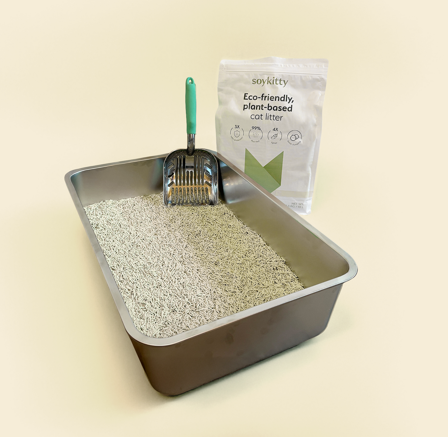 Metal litter box filled with SoyKitty unscented plant-based cat litter and a scoop, with a SoyKitty bag in the background.