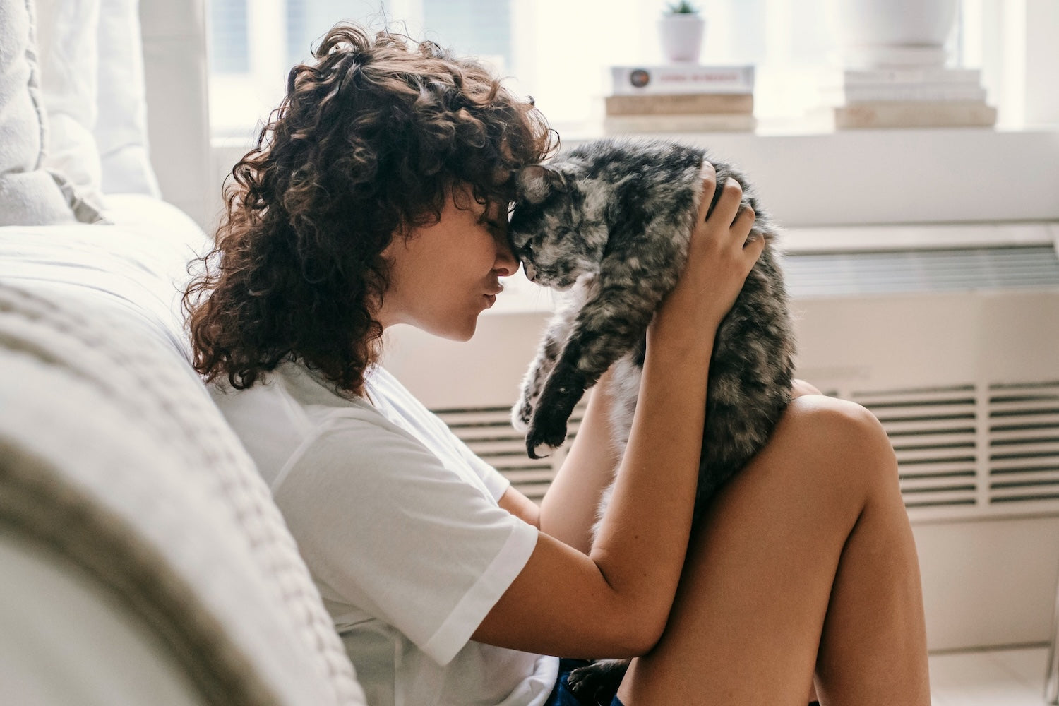 A woman with curly hair holds her cat lovingly in a bright living room