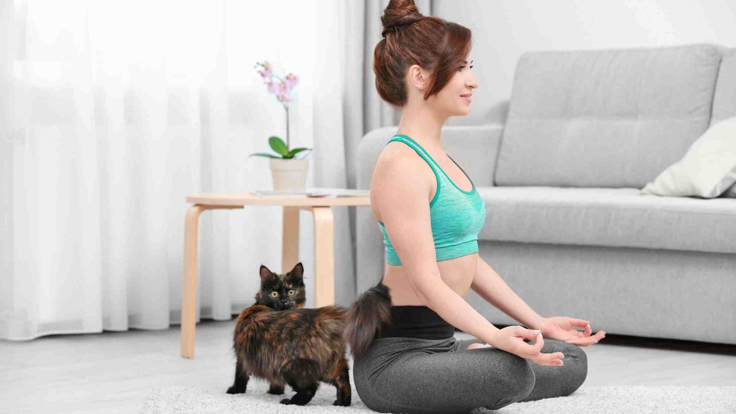 Woman embracing a holistic lifestyle for cats by meditating in a yoga pose with her attentive feline companion at home.