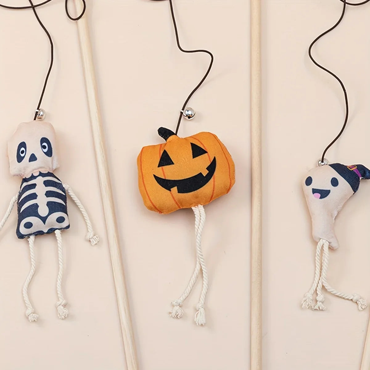 Halloween-themed plush toys including a skeleton, pumpkin, and ghost on strings against a beige background.