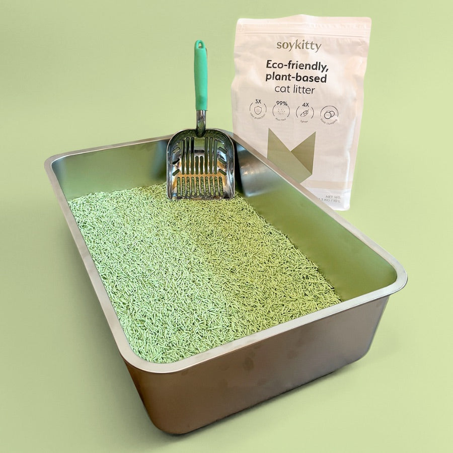 A metal litter box filled with SoyKitty’s biodegradable cat litter, with a scooper and product bag in the background, showcasing odor control and sustainability.